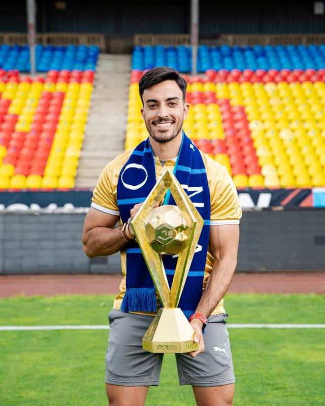 Juan en un estadio, con un trofeo y la bufanda del equipo